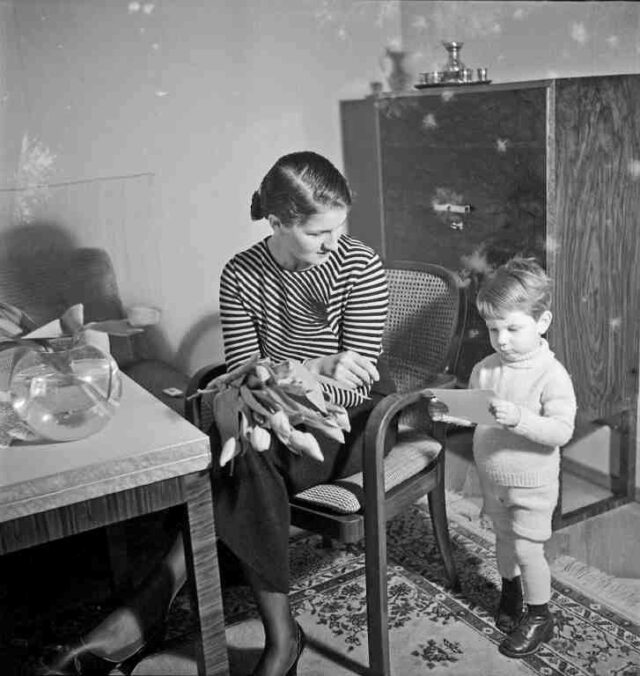 Frau Eberschweiler mit ca. 2jährigem Bub, Tulpen in der Hand, im Wohnzimmer