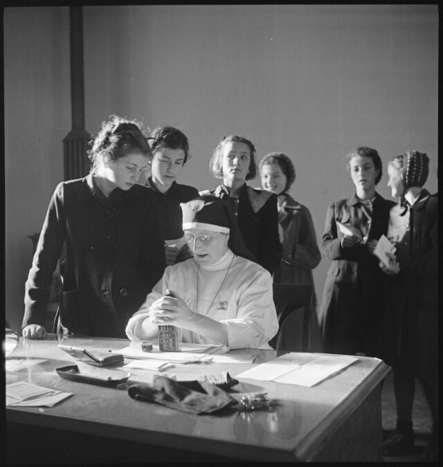 R682: Ordensschwester an Tisch sitzend, Mädchen darum stehend 1
