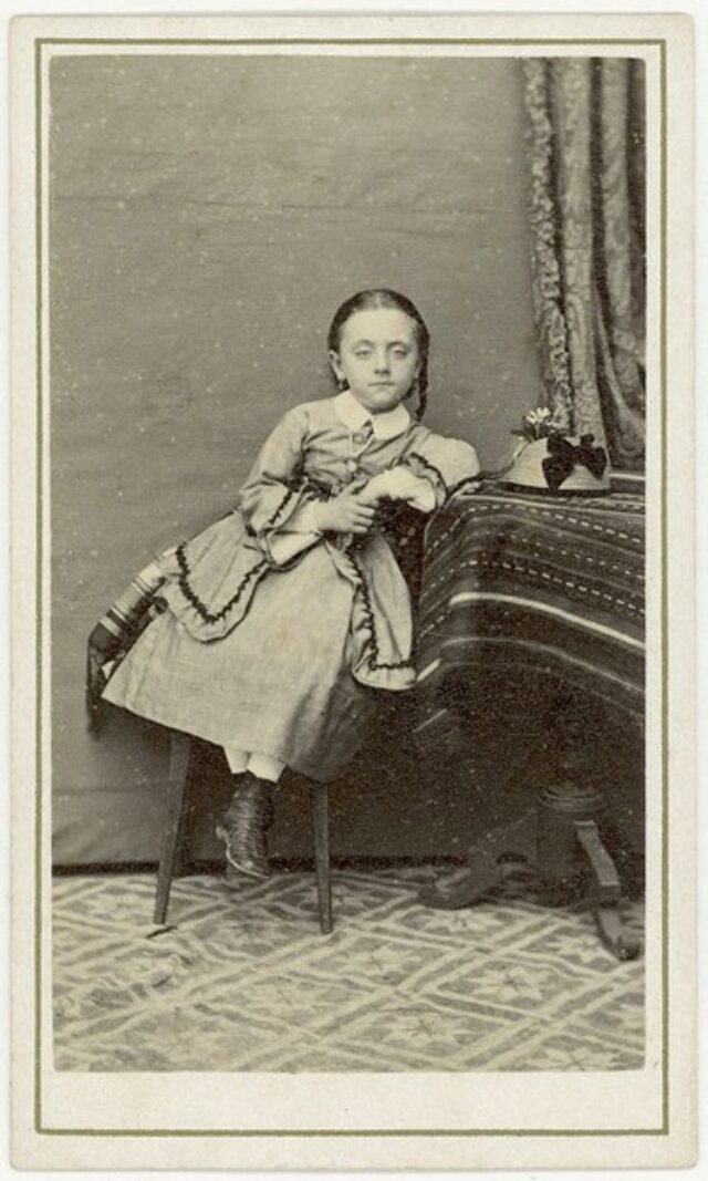 Bambina seduta e appoggiata al tavolo, con cappellino