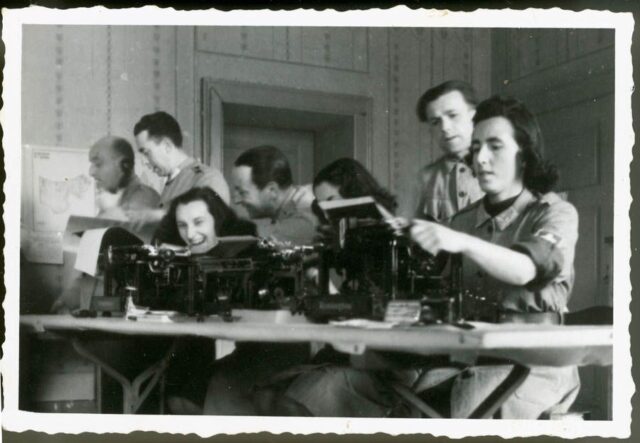 Tre donne e quattro uomini in un ufficio con macchine da scrivere
