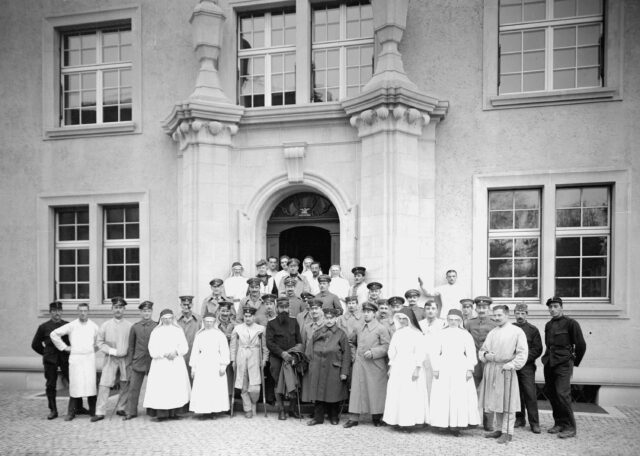 Eine Gruppe deutscher Internierter zusammen mit Krankenschwestern vor dem Portal der Armeesanitätsanstalt