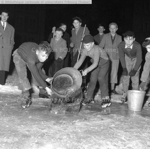 Fribourg, Auge, devant les Augustins: l'arrosage de la patinoire. L'eau est puisée à la fontaine voisine. Et le gel ou le dégel feront leur oeuvre