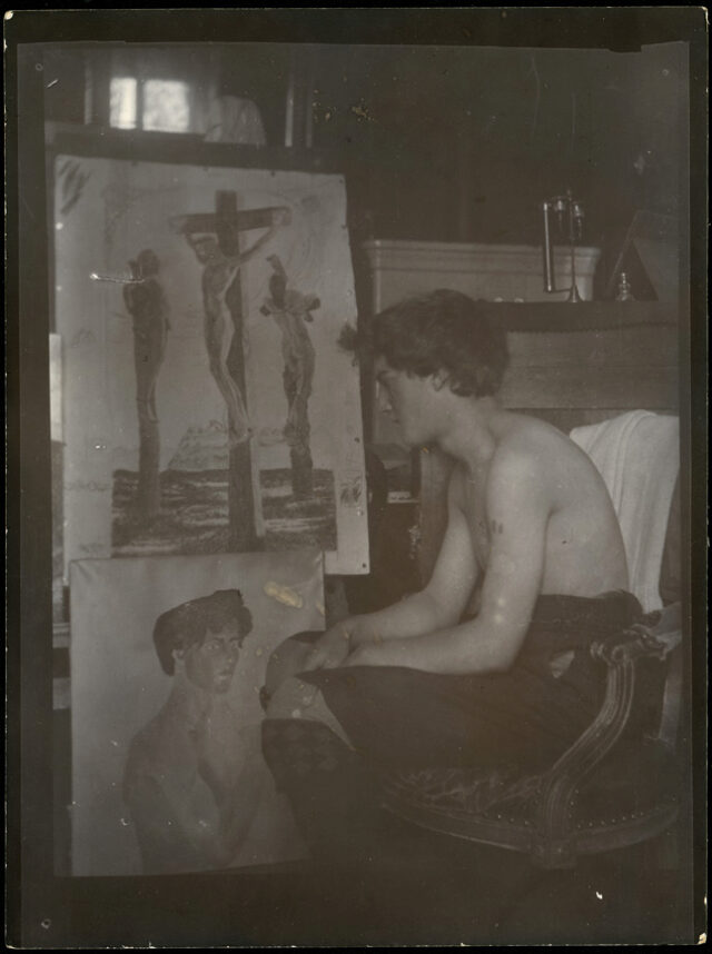 Mario Segantini, torse nu, regardant un tableau