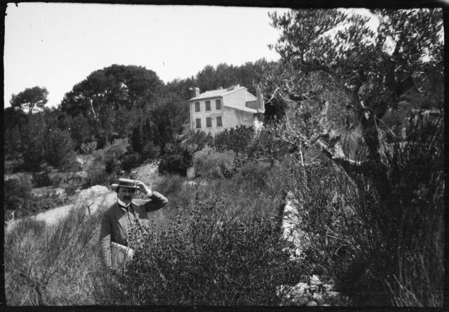 William Ritter, avec son matériel de peinture, dans un champ devant une maison à Aix-en-Provence