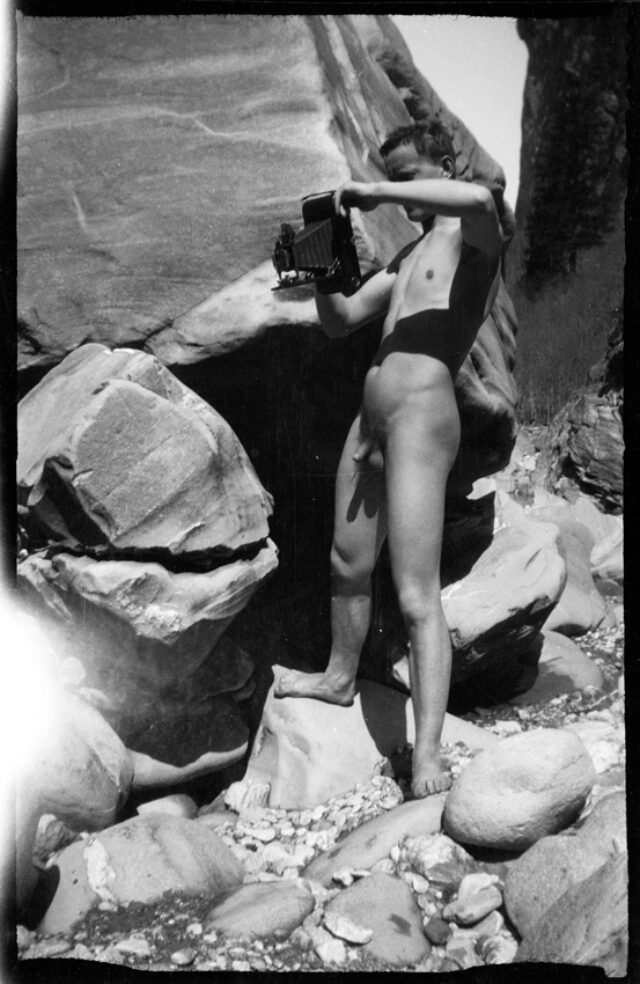 Josef Tcherv, nu, prenant une photographie debout dans les rochers