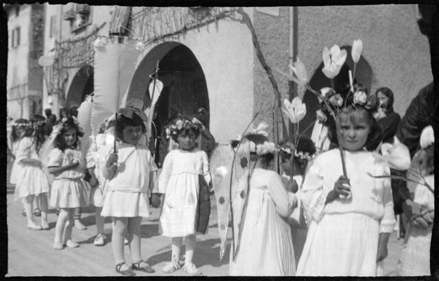 Petites filles se tenant la main et portant des fleurs lors d'un cortège catholique dans les rues d'un village tessinois