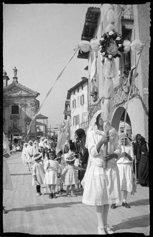 Jeune fille tenant une croix et suivie d'enfants se tenant par la main lors d'un cortège catholique dans les rues d'un village tessinois