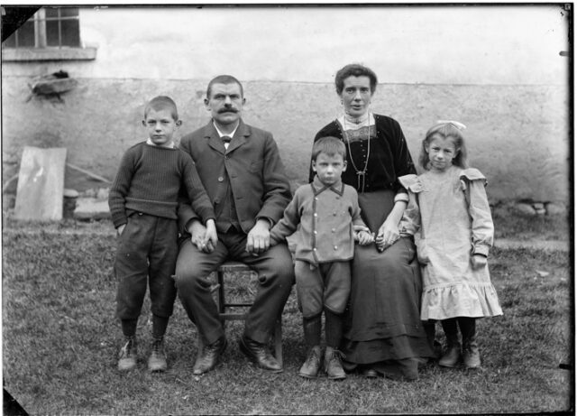 Famiglia Frusetta davanti a un edificio, uomo seduto Martino Frusetta