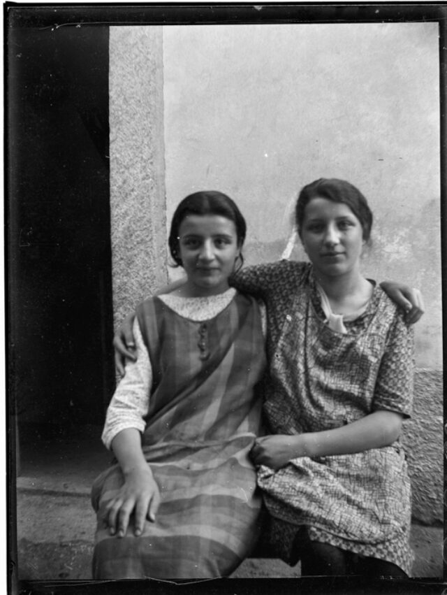 Due ragazze sedute davanti a un muro, a sinistra una delle sorelle Pezzati