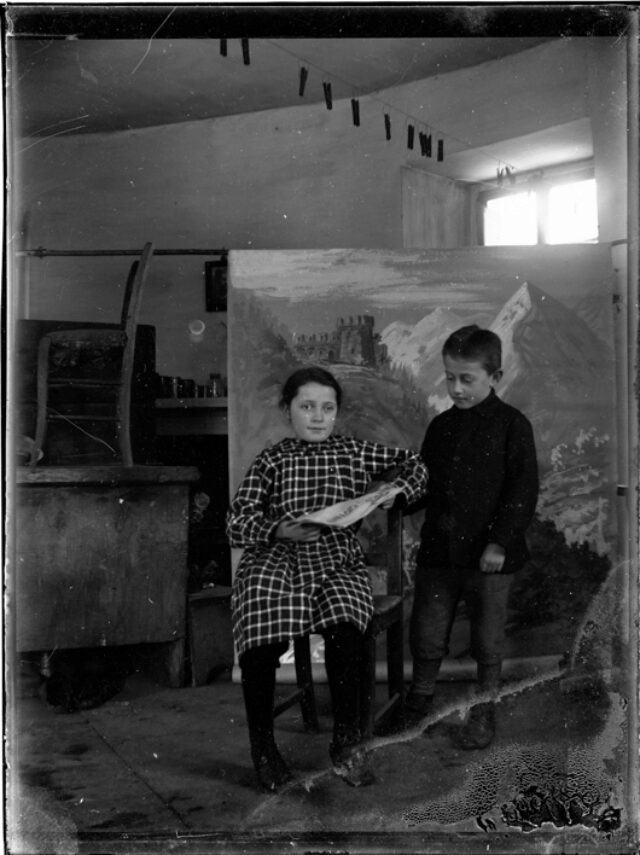 Sibilla Donetta seduta e bambino in piedi all'interno della Casa Rotonda con fondale dipinto