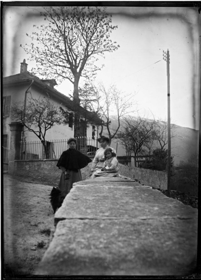 Due donne e una bambina con un cane su un muretto accanto alla strada