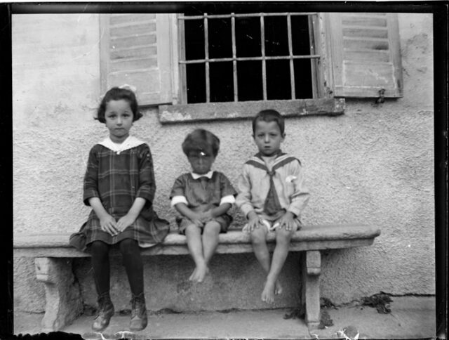 Tre bambini seduti su una panca davanti a una casa