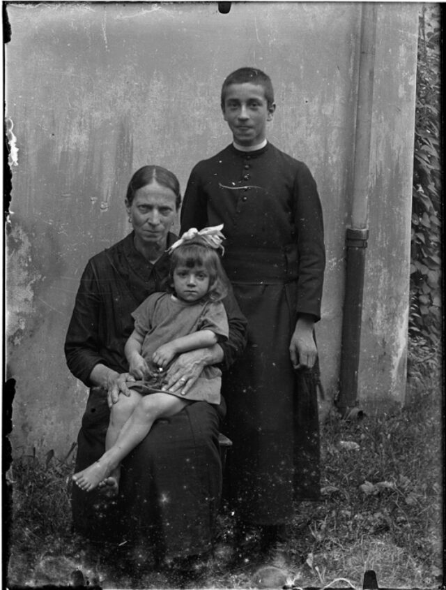 Gruppo di famiglia, donna seduta con bambina in braccio e ragazzo alle spalle, seminarista