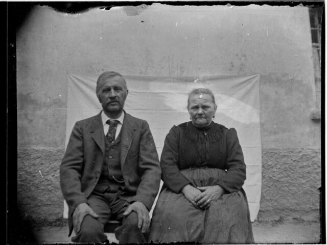 Clemente e Antonietta Bozzini seduti davanti a un telo appeso al muro di una casa