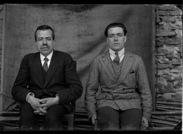 Due uomini, i fratelli Del Bue, seduti davanti ad un telo quale sfondo
