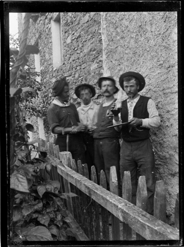 Quattro uomini con cappello dietro una staccionata