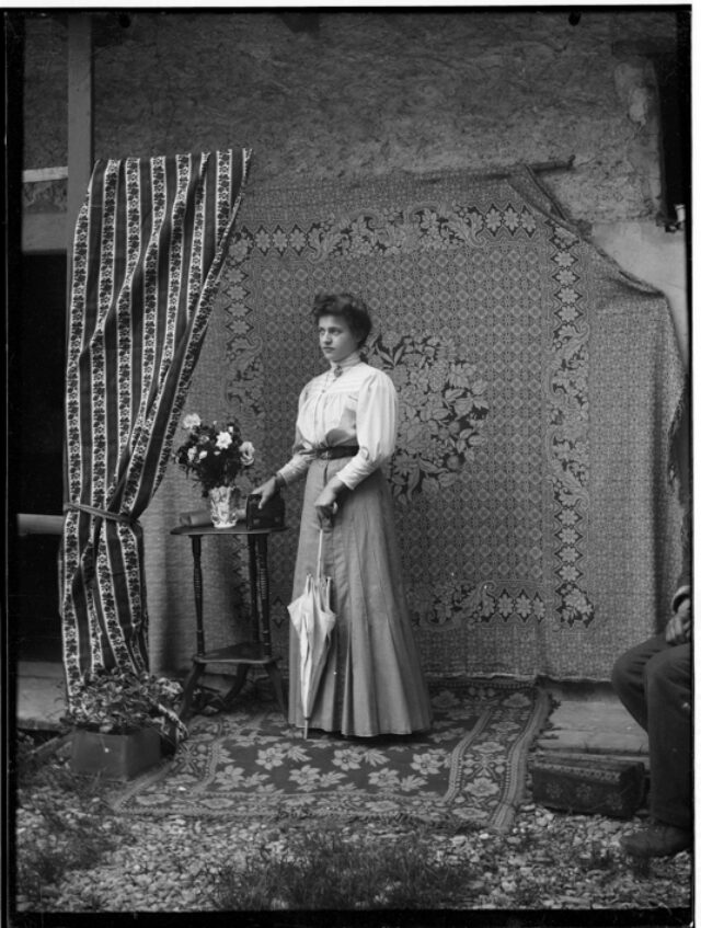 Una figlia di Donetta con abito elegante appoggiata a un tavolino davanti a un drappo a motivo floreale