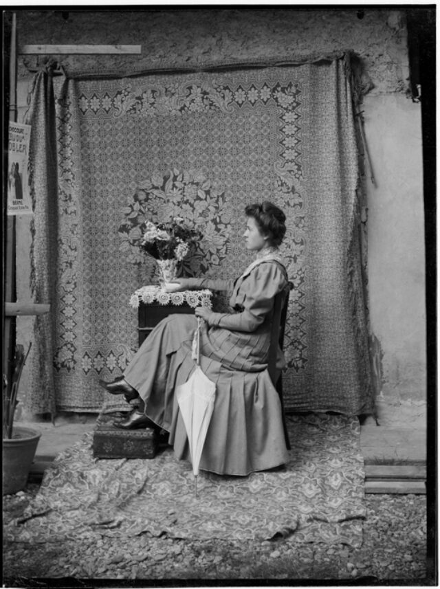 Una Figlia di Donetta seduta di profilo davanti a un fondale con motivo floreale
