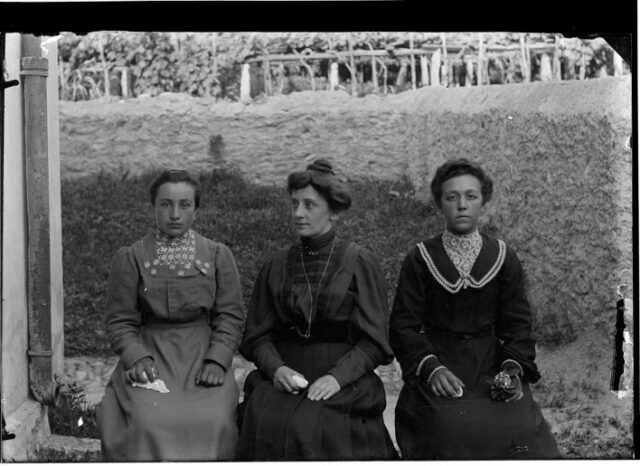 Tre donne sedute su un muretto, con un fazzoletto in mano