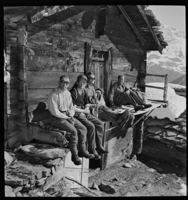 [Eine Gruppe von Grenzwächtern mit Sonnenbrillen bei einer Pause vor einer Berghütte in der Sonne sitzend]