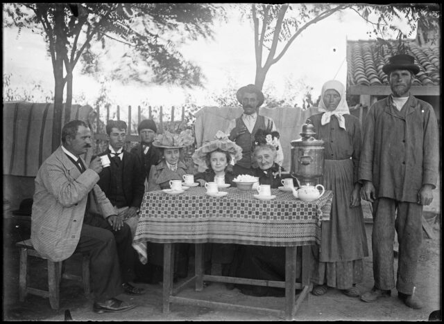 Famille roumaine attablée autour du goûter avec les domestiques en arrière-plan