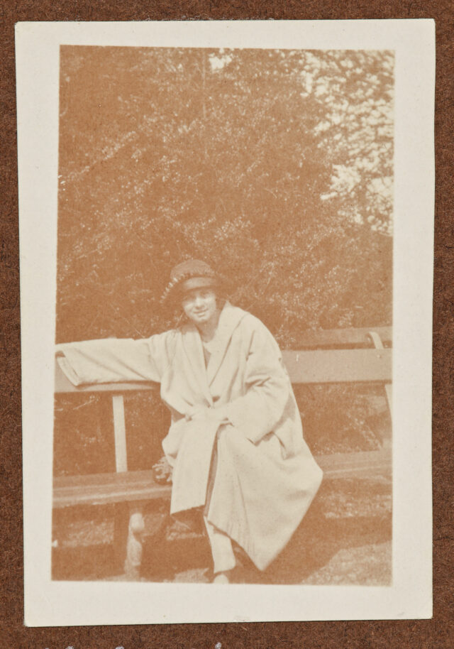 Bettina Zweifel (?) in Mantel und Hut auf einer Bank