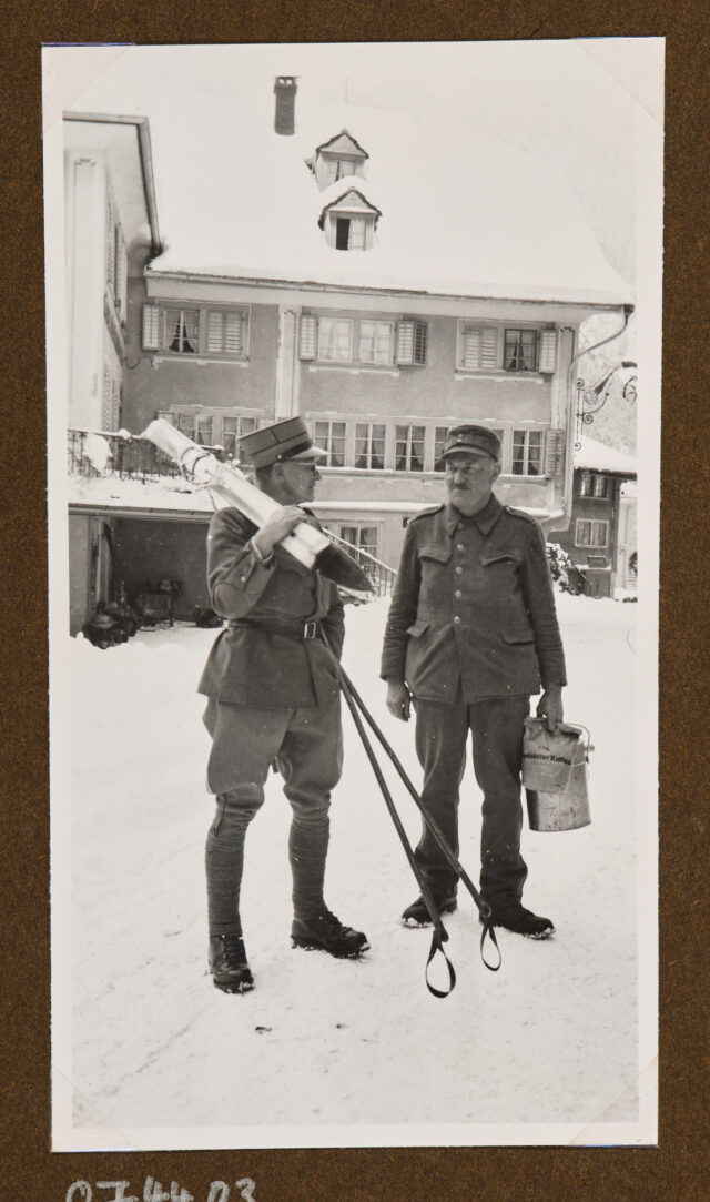 Zwei Soldaten auf Dorfplatz im Schnee, der linke(E. Friedli?) mit Skiern auf der Schulter