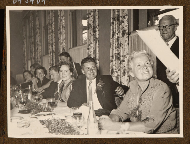 Bettina Zweifel (vorne) und andere Hochzeitsgäste lauschen einer Tischrede (wahrscheinlich von Meinrad Inglin)