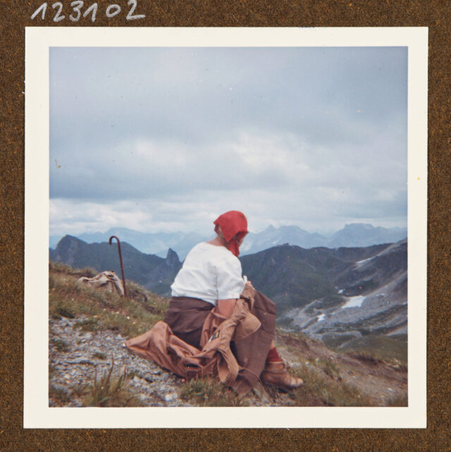 Bettina Zweifel (Rückenansicht) mit rotem Kopftuch vor Bergpanorama