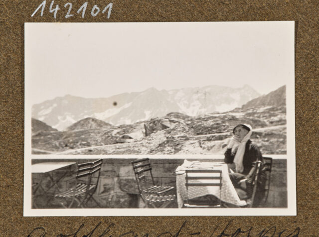 Frau mit Hut an Tisch vor Bergpanorama