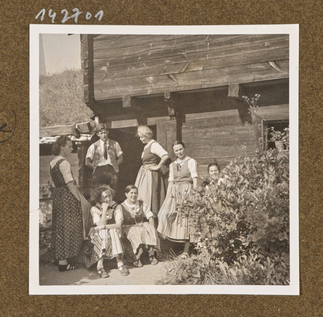 Sieben Personen mit Trachten (Bettina Zweifel hinten Mitte) vor altem Haus