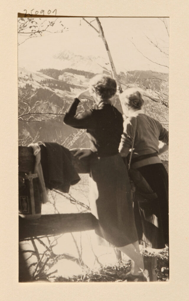 Zwei Frauen (Rückenansicht, vermutlich Helen Weber und Bettina Zweifel) an Geländer vor Bergpanorama
