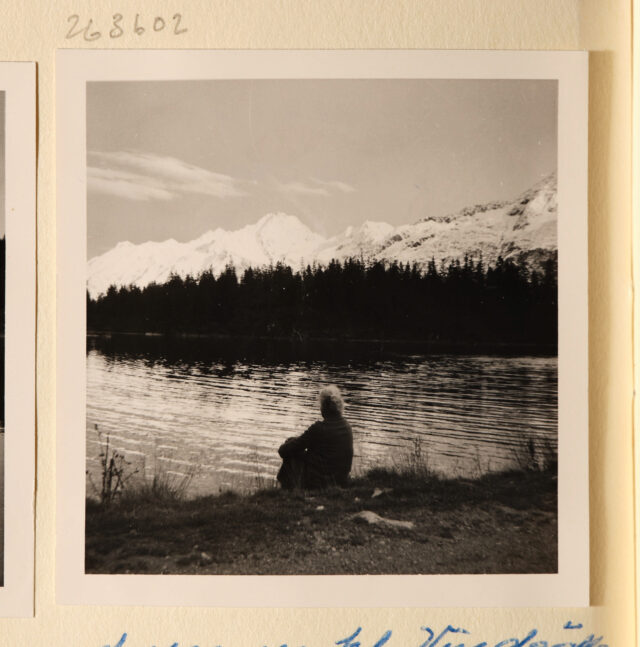 Bettina Zweifel (Rückenansicht) an Bergsee sitzend