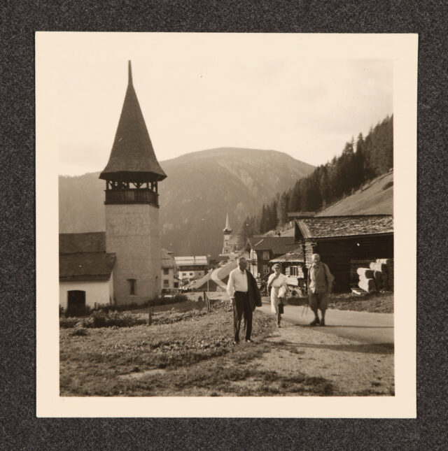 Meinrad Inglin (r.) und zwei weitere Personen (vermutl. Emil u. Anny Holdener) vor Dorf mit Kirche