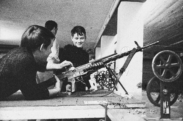 "Freizeitanlagen, Gemeinschaftszentren: Schiessanlage FZA Bachwiesen, Zürich" - Junge lädt liegend ein Gewehr, anderer Junge schaut zu; um 1970