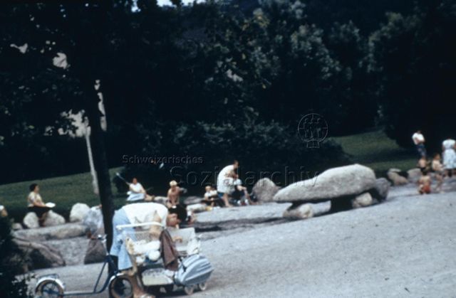 "Freizeitanlagen, Gemeinschaftszentren: Spielplatz Bachwiesen, Zürich" - Frau bückt sich zu einem Kind im Kinderwagen; um 1960
