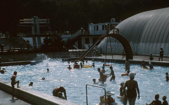 "Europäische Länder: Freibad und Schwimmhalle, Revierpark Nienhausen" - Ansicht des Nichtschwimmerbeckens mit Rutschbahn, zahlreiche Kinder sind am Baden, einige Personen tragen eine Schwimmhaube; um 1970