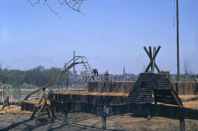 "Europäische Länder: Revierpark Gysenberg Herne, Deutschland" - Kinderspielplatz mit Bauten aus Holz und langer Rutschbahn in einem Park mit Sportplatz; um 1970