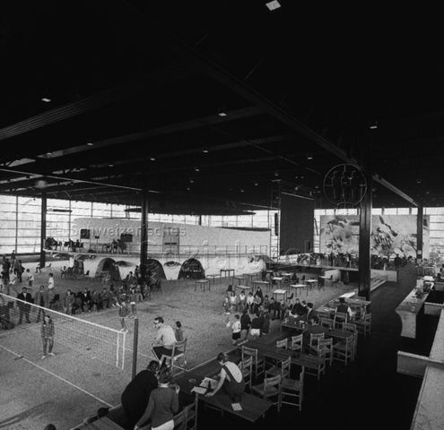 "Europäische Länder: Dronten Holland" - In der grossen, industriell anmutenden Halle wurde ein Volleyballnetz gespannt, Galerie mit Tischen und Stühlen, im Hintergrund das runde Gebäude mit durchgebendem Balkon; um 1970