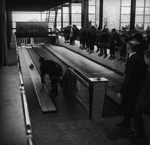 "Europäische Länder: Dronten Holland" - Kegelbahn in der industriell anmutenden Halle, Männer kegeln, Jugendliche sitzen auf einer Mauer und schauen zu; um 1970