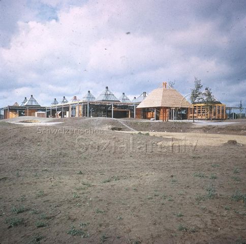"Europäische Länder: Gemeinschaftszentrum, Eindhoven Holland" - Baustelle von einstöckigen Holzhäusern mit spitzen Dächern in ländlichem Umfeld; um 1970