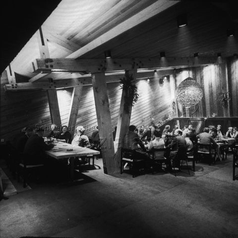 "Europäische Länder: Dronten, Holland" - Innenraum mit sichtbaren Holzbalken, Frauen und Männer in Anzügen sitzen an Tischen und unterhalten sich miteinander; um 1970
