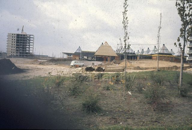"Europäische Länder: Zentrum Eindhoven, Holland" - Baustelle von einstöckigen Holzhäusern mit spitzen Dächern in ländlichem Umfeld, daneben wird ein Wohnblock gebaut; um 1970