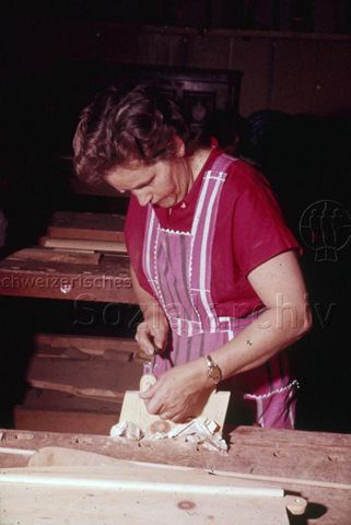 "Schreinern: Frau an Hobelbank" - Eine Frau steht an der Werkbank, ganz in ihre Holzarbeit vertieft, sie trägt eine Schürze; um 1970
