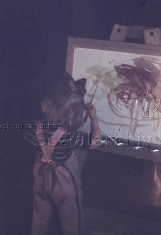 "Zeichnen und Malen: Erste Malkunst" - Ein kleines Mädchen steht an einer Staffelei und malt mit Wasserfarben, sie trägt eine Schürze; um 1960