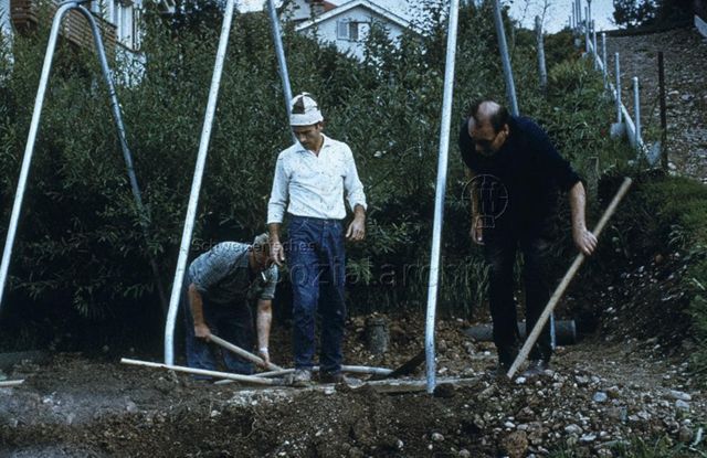 "Siedlungs- und Quartierspielplätze: Lichtensteig SG" - Drei Männer beim Hacken und Schaufeln unter einem Schaukelgerüst; um 1970