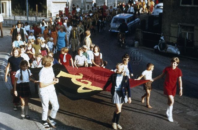 "Siedlungs- und Quartierspielplätze: Lichtensteig SG" - Strassenumzug von Kindern, sie tragen eine Fahne; um 1970
