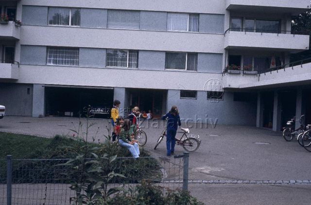 "Siedlungs- und Quartierspielplätze: Lichtensteig SG" - Kinder spielen auf dem Parkplatz vor einem Wohnhaus; um 1970