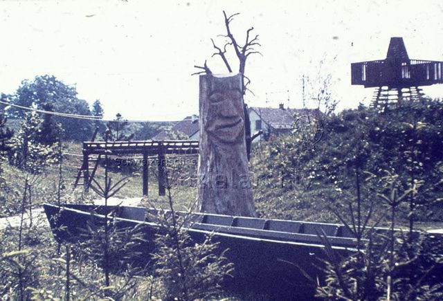 "Siedlungs- und Quartierspielplätze: Siedlungsspielplatz Möhlin AG, 1975" - Spielplatz mit hölzernem Turm, Klettergerüst und Boot, in der Mitte ein Baumstrunk, in den ein Gesicht geschnitzt wurde
