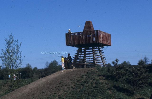 "Siedlungs- und Quartierspielplätze: Siedlungsspielplatz Schalle/ Möhlin AG, 1976" - Kinder spielen um einen aus Holz gebauten Turm im Grünen